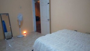 A bedroom with a bed, a standing fan, and a door leading to another room. - Relax and enjoy in this beautiful home in a quiet neighbourhood. (Mineral Hieghts)