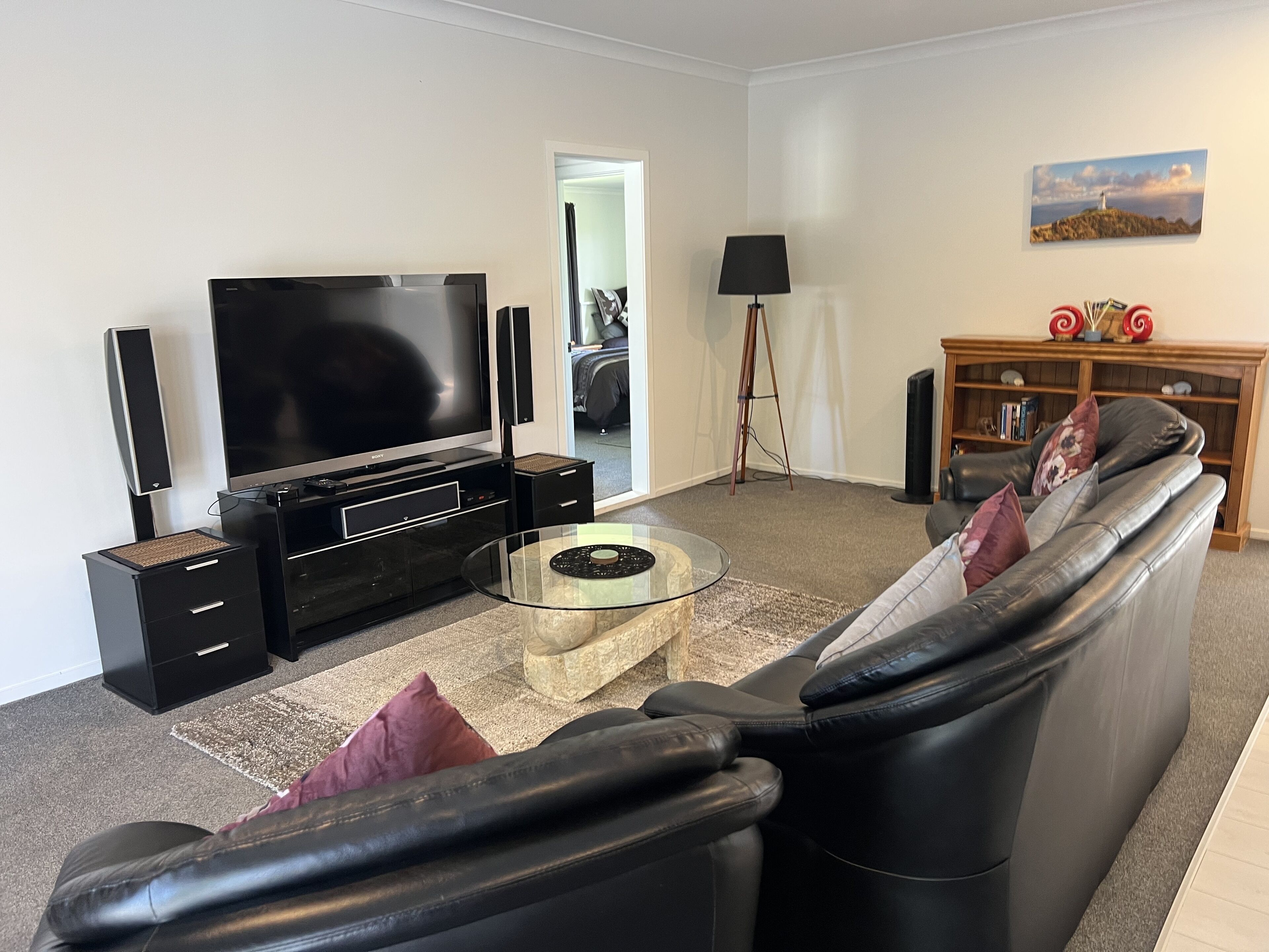 Uma sala de estar moderna com televisão de tela plana, unidade de entretenimento preta, mesa de centro de vidro, sofá de couro e uma estante.