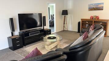 Uma sala de estar moderna com televisão de tela plana, unidade de entretenimento preta, mesa de centro de vidro, sofá de couro e uma estante.