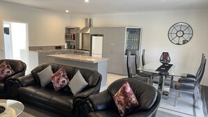 A modern living room with a black leather sofa set, a glass coffee table, and a dining area with a glass table and chairs.