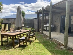 A patio with a wooden table and chairs, a grill, and a covered area with a fence. - A Cut Above - gateway to the Bay of Islands (Kerikeri)
