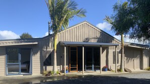 A modern building with a covered entrance, large sliding glass doors, and a gravel driveway.