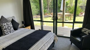 A bedroom with a large bed, a chair, and a view of a garden through a glass door.