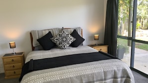 A bedroom with a large bed, two bedside tables, a nightstand, and a window with a view of greenery.