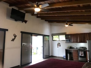 Un vaste espace de vie avec une grande porte-fenêtre coulissante donnant sur un balcon, une cuisine dotée de meubles en bois et un ventilateur de plafond.
