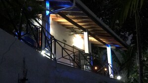 A staircase with a wooden handrail and metal railings, leading to a building with a white exterior and blue lighting accents. - Villas Lambeau #2 - Ocean View - Fiber Optic / 1BR 1 BA (Uvita)
