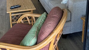 Een woonkamer met een grijze bank, rieten meubels en een afstandsbediening op een houten tafel.