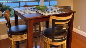 A dining area with a table set for four, two chairs on each side, a view of the ocean through large windows, and a lobster-themed artwork on the wall. - Oceanfront Retreat. Sunset Views. Whale Watching. Redwood Groves, 2 King Beds (Crescent City)