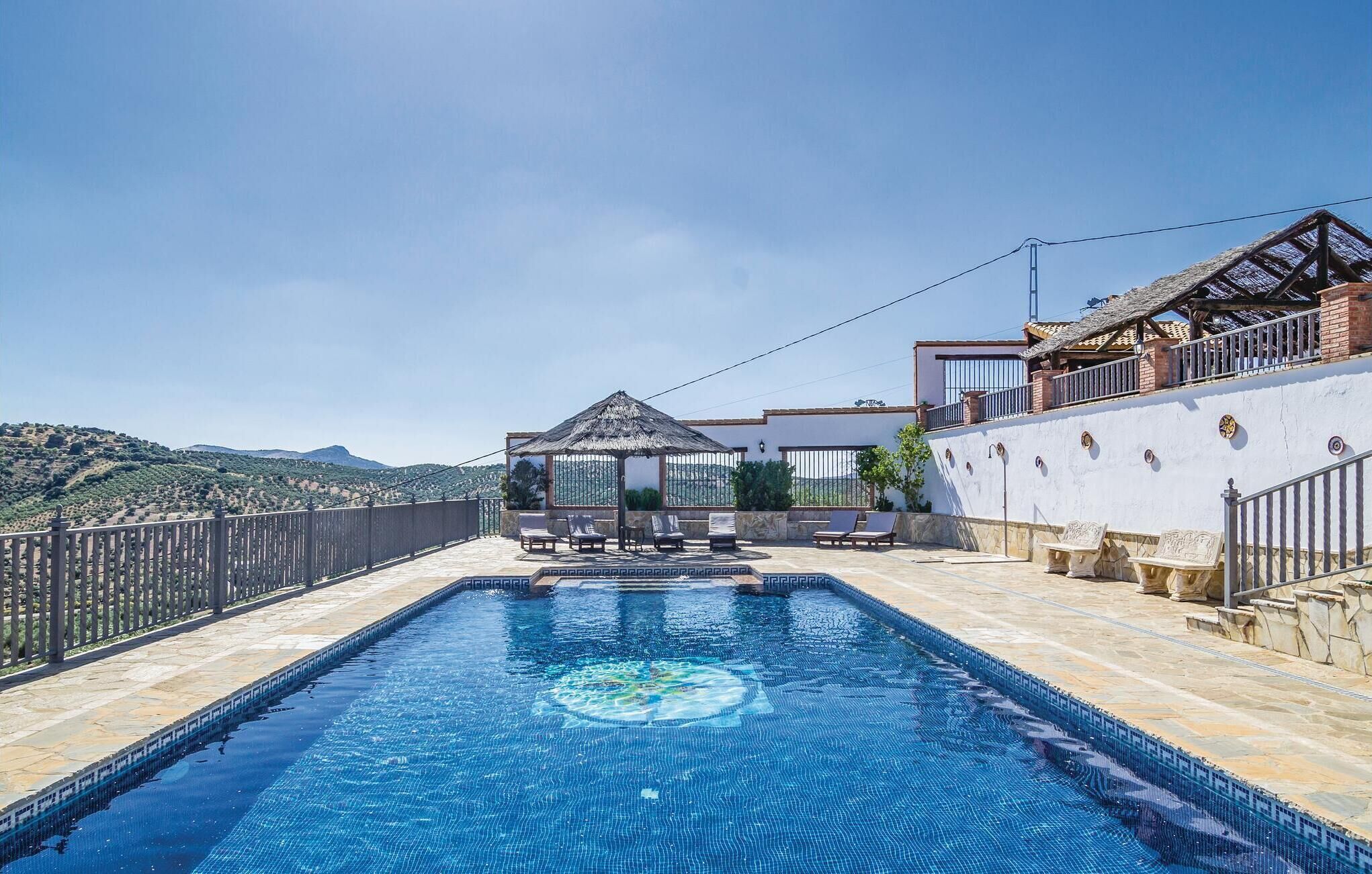 Una piscina con vistas a las colinas, un área de estar techada y un edificio con techo de tejas.