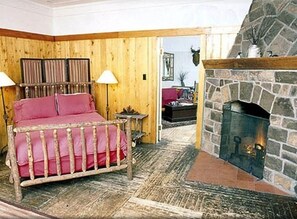A cozy room with a bed, a stone fireplace, and wooden walls. - Premier Cabin 1 with Lake View (Paul Smiths)