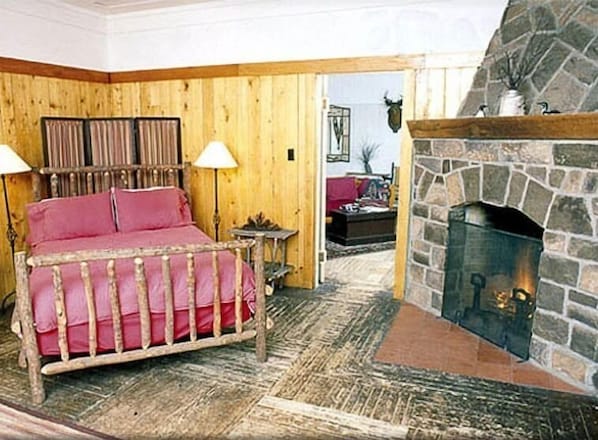 A cozy room with a bed, a stone fireplace, and wooden walls. - Premier Cabin 1 with Lake View (Paul Smiths)