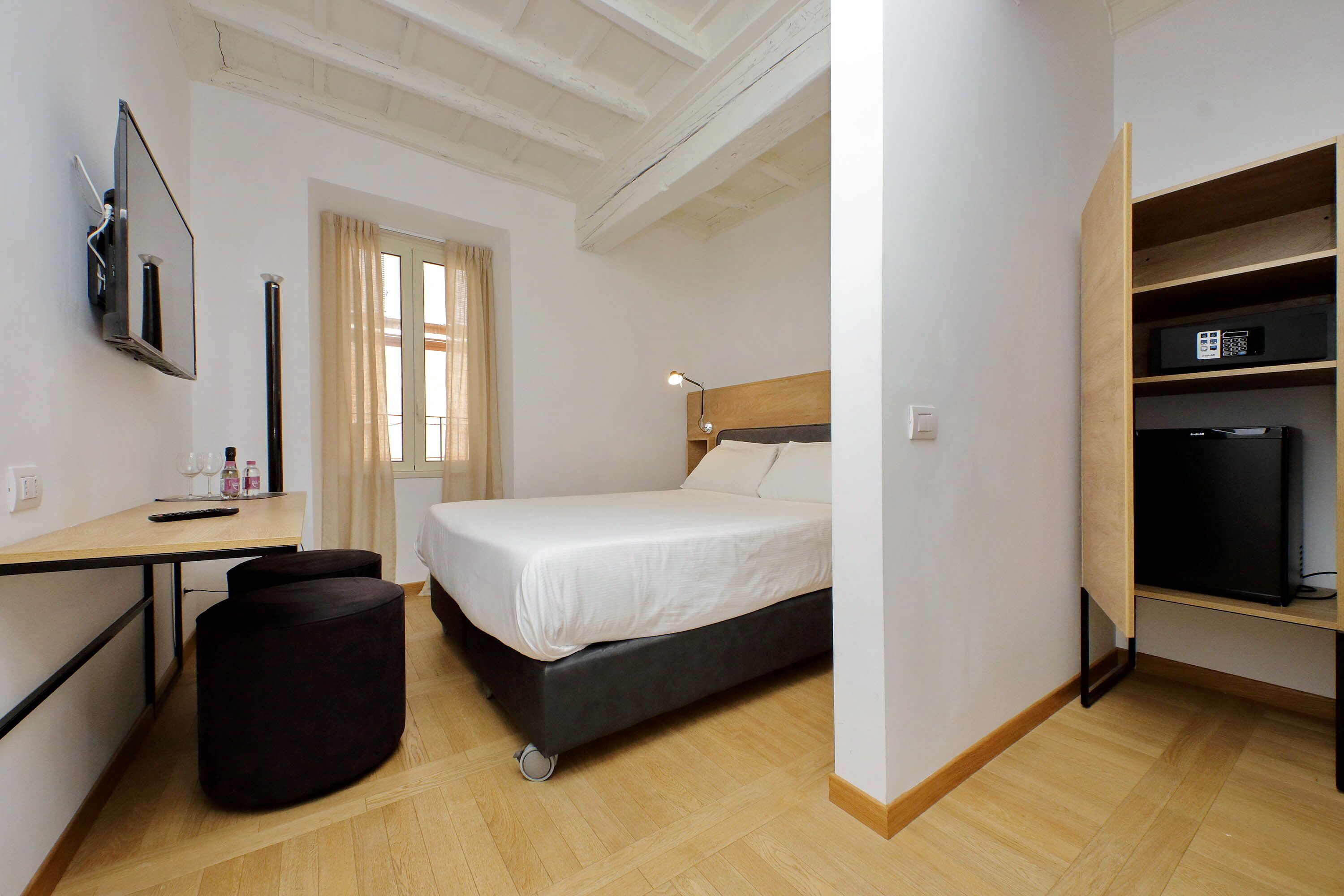 A bedroom with a bed, a desk with a chair, a TV, and a shelf with a TV.