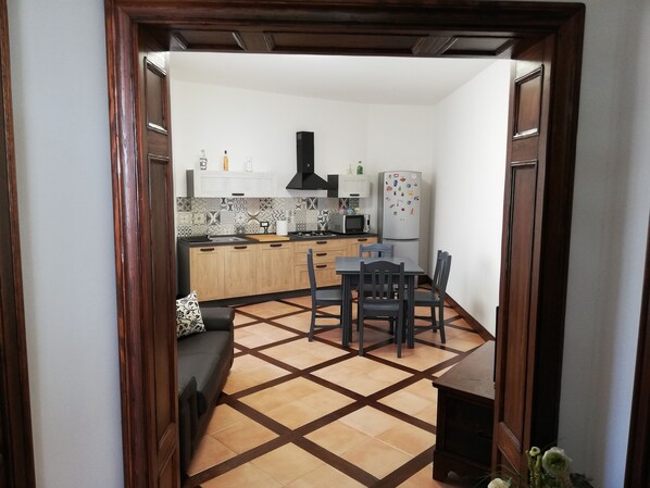 A compact kitchen with wooden cabinets, a dining table with chairs, and a small seating area with a sofa.