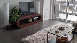 A modern living room with a flat-screen TV, a wooden entertainment unit, a fluffy rug, and a glass door leading to a balcony.