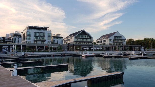 A marina with modern buildings, including a Starbucks, docked boats, and a wooden dock.
