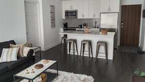 A modern kitchen with white cabinets, a central island with stools, a microwave, and a refrigerator.