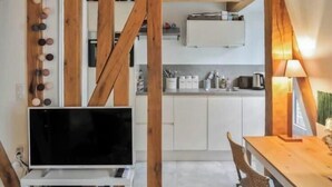 A cozy kitchen with wooden beams, a TV, and a dining area with a table and chairs.