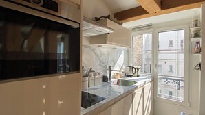 A compact kitchen with a built-in oven, a stovetop, and a window overlooking the street.
