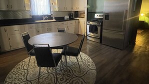 A compact kitchen with a dining table, chairs, a refrigerator, and a stove. - Historical Louisiana Style Home (Dayton)