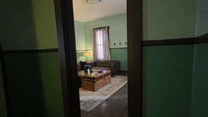 A hallway leading to a living room with a sofa, coffee table, and a lamp. - Historical Louisiana Style Home (Dayton)