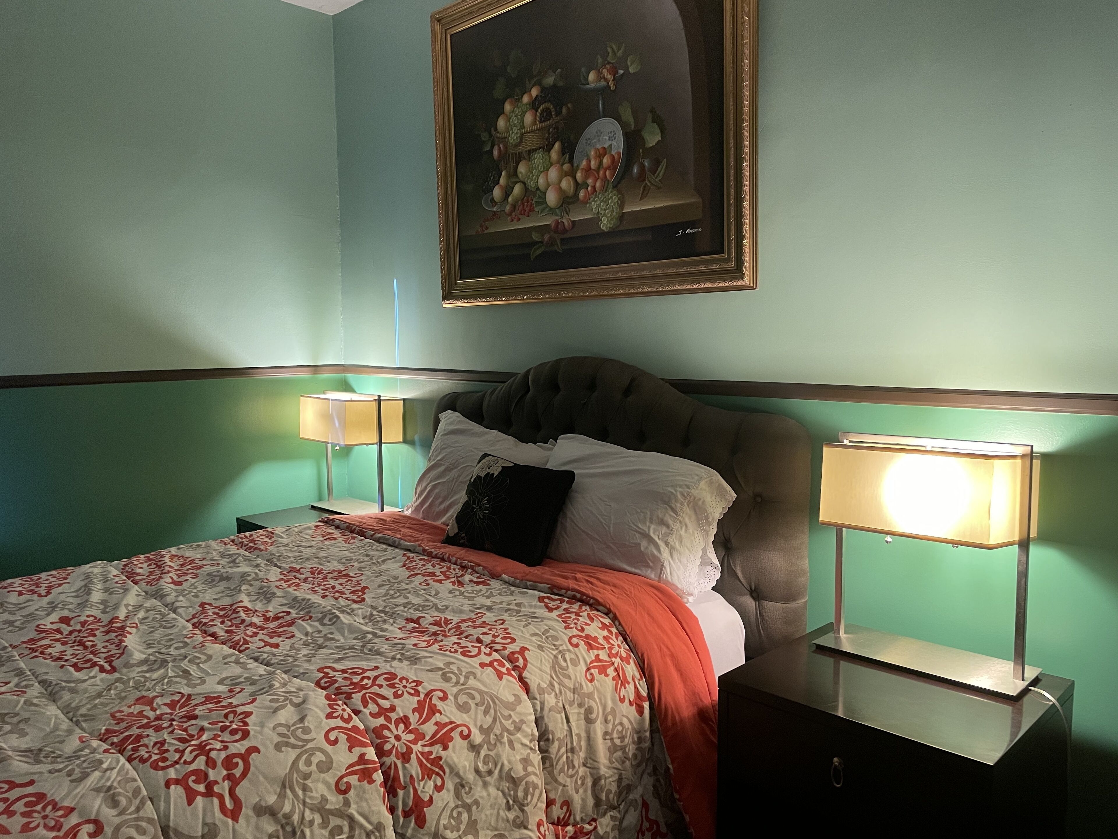 A neatly made bed with a patterned bedspread, two bedside lamps, and a framed painting above the bed.