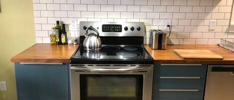 A kitchen with a stainless steel stove, oven, and a kettle on the counter.