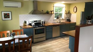 Una cocina con estufa, horno y lavavajillas, sillas de madera y una ventana con plantas.