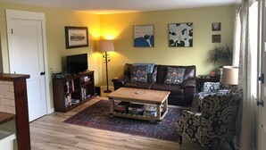 Una sala de estar con un sofá marrón, una mesa de centro, un televisor sobre un mueble bajo y una estantería.