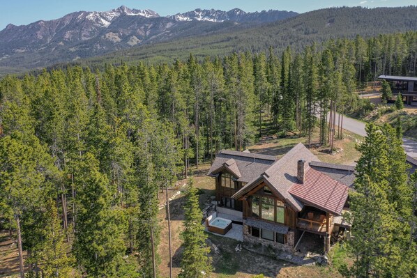 A modern log cabin with a stone foundation, large windows, and a hot tub in front. - Big Sky Vacation Rentals: MVC Spotted Eagle (Big Sky)