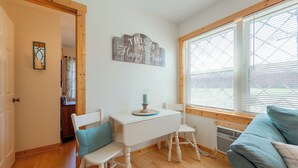 Une pièce chaleureuse avec un plancher en bois, une table blanche avec deux chaises, un canapé bleu et une fenêtre avec des stores.