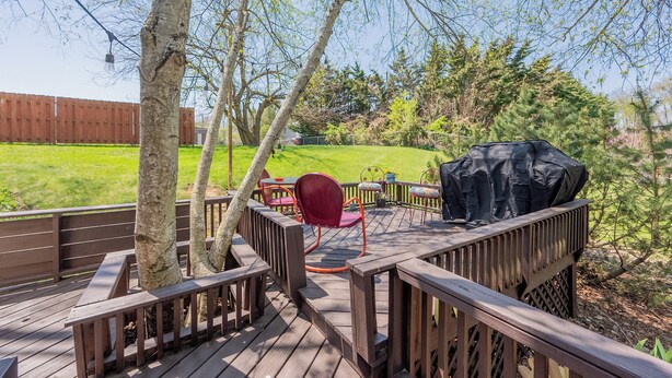 Une terrasse en bois avec un barbecue, une chaise rouge et une table.