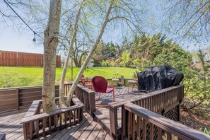 Une terrasse en bois avec un barbecue, une chaise rouge et une table.