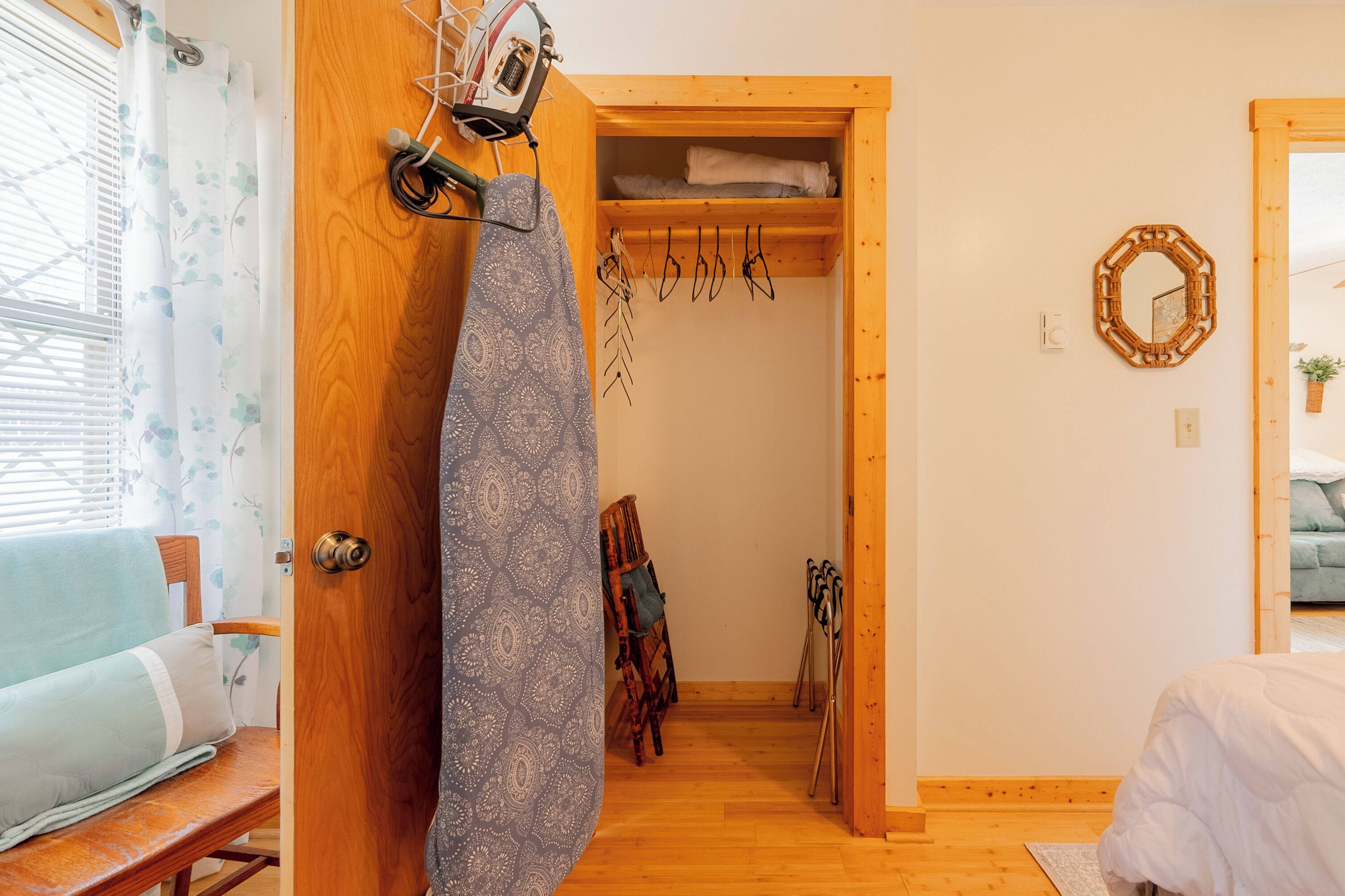 A wooden door leading to a room with a bed, a chair, and a wooden shelf with towels.