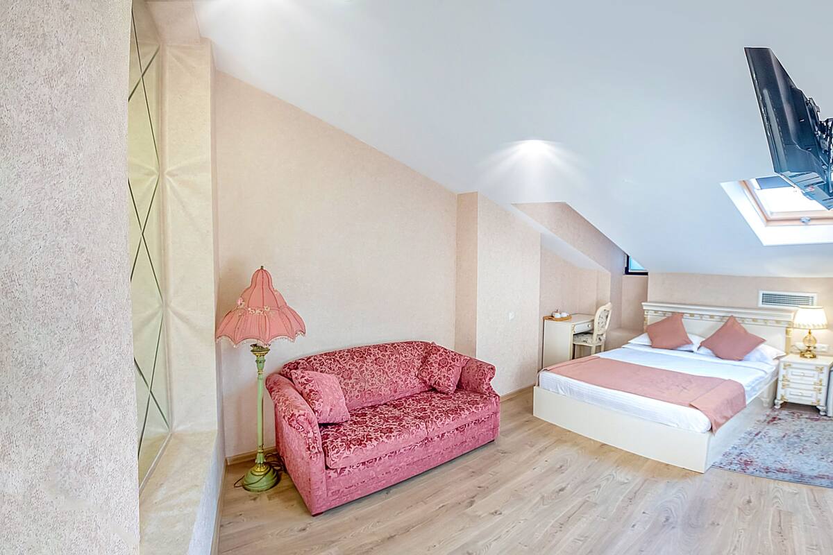 A bedroom with a bed, a red sofa, a lamp, and a desk.