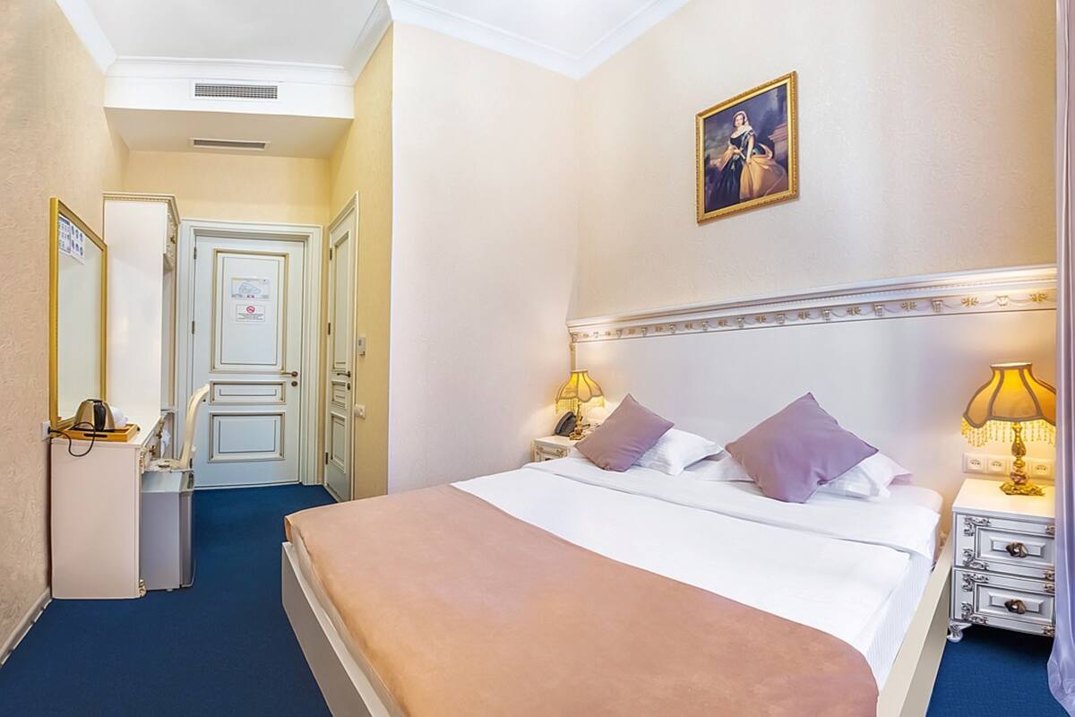 A hotel room with a large bed, two bedside tables with lamps, a mirror, a door, and a framed picture on the wall.