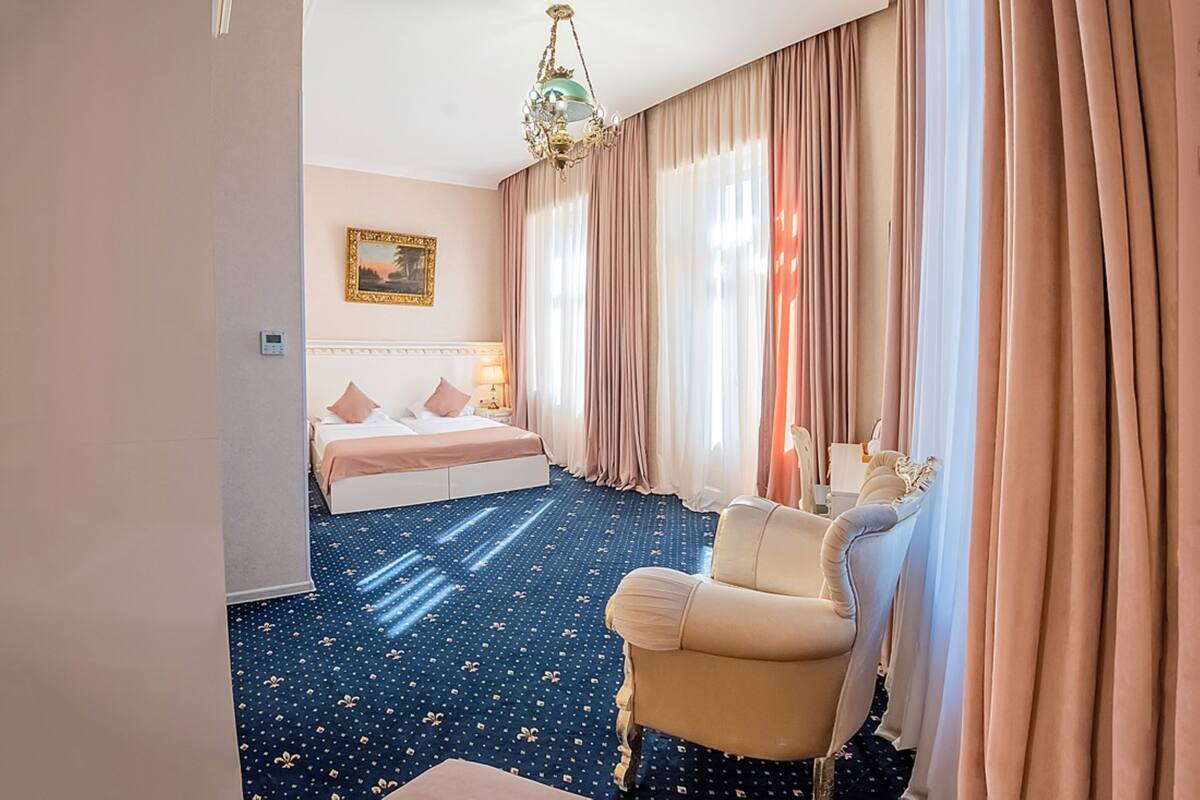 A hotel room with a bed, a chair, a desk, and a chandelier.