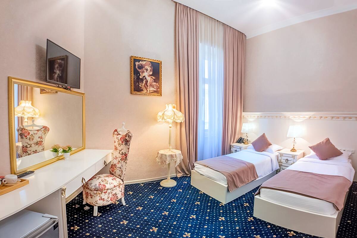 A hotel room with a large mirror, a desk with a lamp, a chair, two beds, and a large window with curtains.
