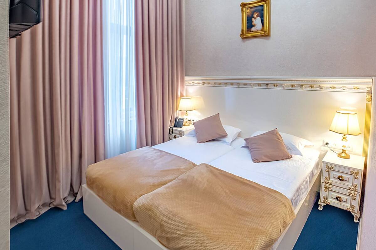 A hotel room with a large bed, a chandelier, a television, and a painting on the wall.