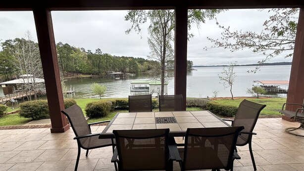 Een terras buiten met een tafel en stoelen, met uitzicht op een meer met boten en een steiger.