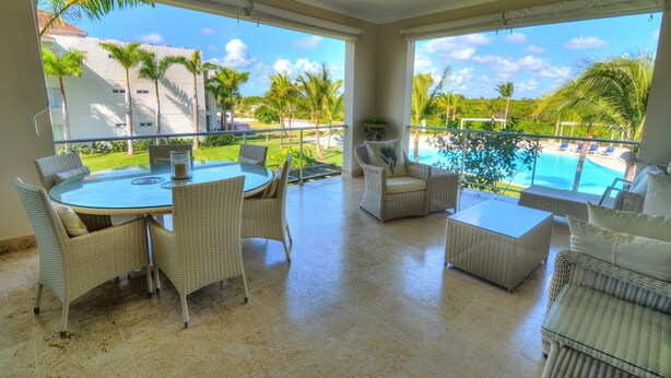 Ein geräumiger Balkon mit Blick auf einen Swimmingpool und Palmen, ausgestattet mit Korbstühlen und einem runden Tisch.