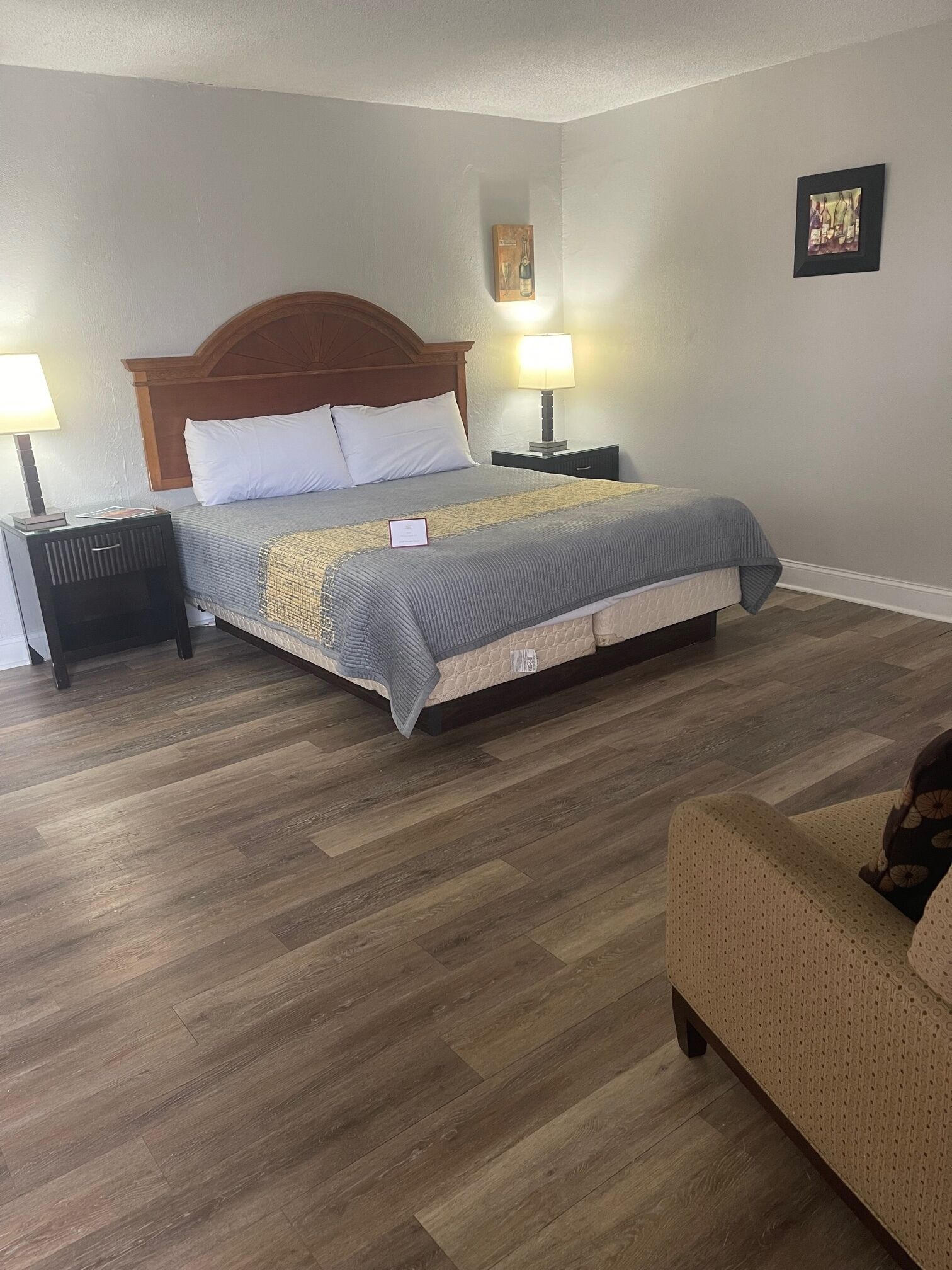 Habitación de hotel ordenada con una cama grande, dos mesitas de noche con lámparas, un cabecero de madera y un sillón pequeño.