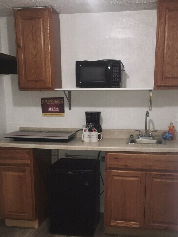 A small kitchenette with wooden cabinets, a microwave, a coffee maker, and a sink.