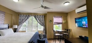 Una habitación de hotel con cama, escritorio, silla, televisor y ventilador de techo.