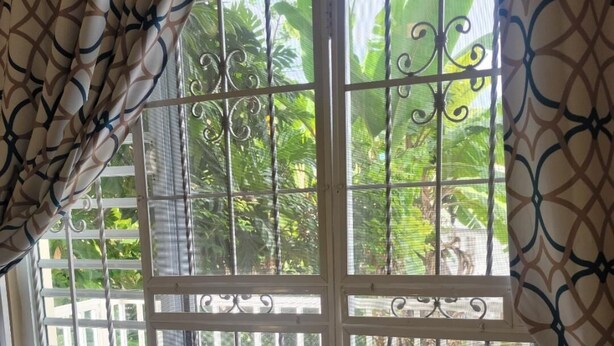 A room with a large window featuring metal bars and a view of a patio area with a table and chairs.