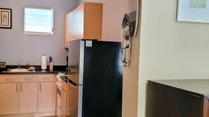 A kitchen with wooden cabinets, a black refrigerator, and a window with blinds.