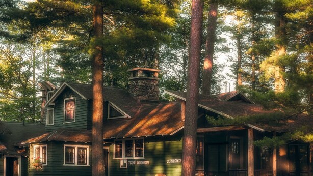 Une cabane rustique avec une cheminée en pierre, une véranda et une enseigne indiquant « Bureau » et « Boutique de cadeaux ».