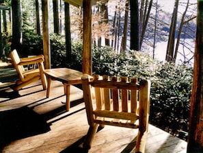 A wooden deck with a table and two chairs, surrounded by trees and bushes.