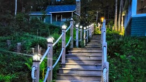 Una escalera de madera con barandillas e iluminación que asciende por una colina rodeada de vegetación.