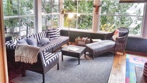 Una habitación acogedora con un sofá, dos sillones, una mesa de centro y vistas a árboles a través de amplias ventanas.