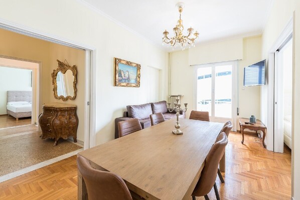 A spacious dining area with a large wooden table, leather chairs, a chandelier, and a painting on the wall.